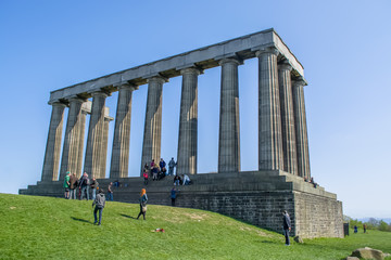 View of National Monument of Scotland, on Calton Hill in Edinburgh, with grass around and people enjoying it