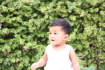 ASEAN children sitting smiling background with green leaves.  8 months old.
