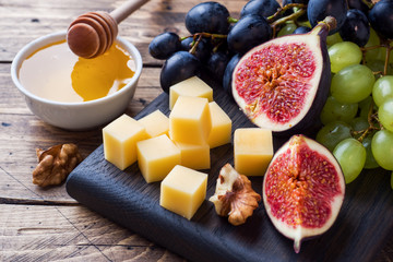 Cheese cubes, fresh fruit figs grapes Honey walnut on wooden chopping Board. Selective focus. Close up.