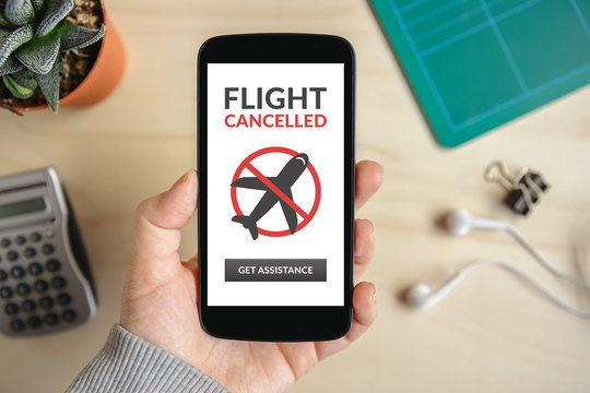 Hand holding smart phone with flight cancelled concept on screen. Top view