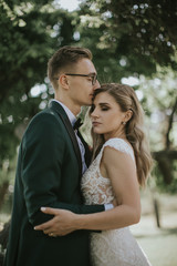 Portrait of a lovely bride and groom embrace, kiss and hug each other. Couple in love in the bosom of nature . Handsome groom and beautiful blonde bride posing in the forest. Modern dress and suit