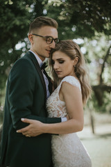 Portrait of a lovely bride and groom embrace, kiss and hug each other. Couple in love in the bosom of nature . Handsome groom and beautiful blonde bride posing in the forest. Modern dress and suit