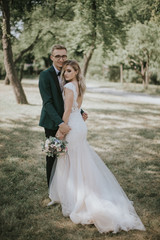 Fototapeta na wymiar Portrait of a lovely bride and groom embrace, kiss and hug each other. Couple in love in the bosom of nature . Handsome groom and beautiful blonde bride posing in the forest. Modern dress and suit