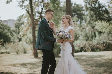 Naklejka premium Portrait of a lovely bride and groom embrace, kiss and hug each other. Couple in love in the bosom of nature . Handsome groom and beautiful blonde bride posing in the forest. Modern dress and suit