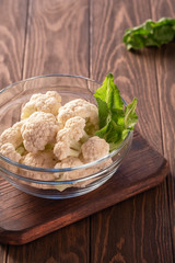 Fresh cauliflower with green leaves in a glass cup on a wooden board