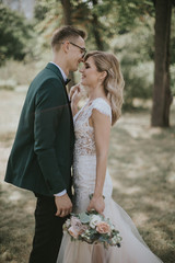 Portrait of a lovely bride and groom embrace, kiss and hug each other. Couple in love in the bosom of nature . Handsome groom and beautiful blonde bride posing in the forest. Modern dress and suit