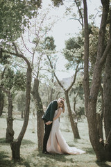 Portrait of a lovely bride and groom embrace, kiss and hug each other. Couple in love in the bosom of nature . Handsome groom and beautiful blonde bride posing in the forest. Modern dress and suit