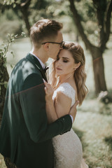 Portrait of a lovely bride and groom embrace, kiss and hug each other. Couple in love in the bosom of nature . Handsome groom and beautiful blonde bride posing in the forest. Modern dress and suit