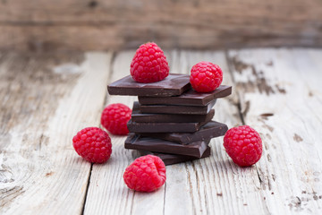 Dark chocolate stack with fresh raspberries, on wooden table. Natural light, selective focus.
