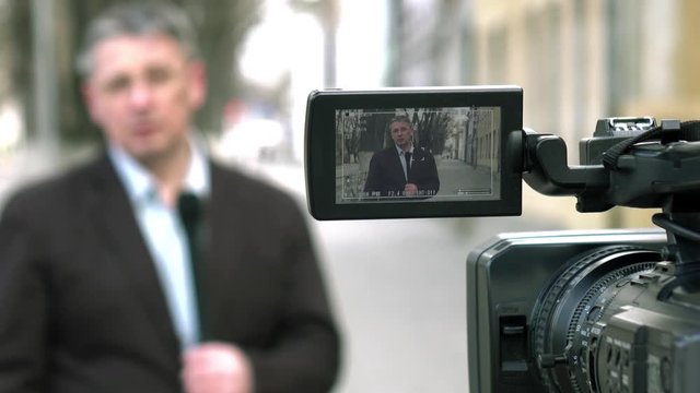 A middle-aged European journalist is reporting on a city street.