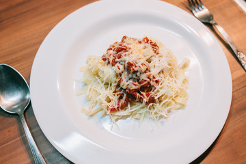 Delicious plate of pasta bolognese with a cheese served on the wooden table and prepared to eat. Italian kitchen. Studying culinary online.