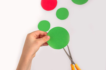 Concept of DIY and children's creativity. Step by step instruction: how to make applique frog from paper. Step 2 child holds paper circle and scissors. Creative activities with child during quarantine