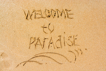 welcome to paradise written in the sandy beach