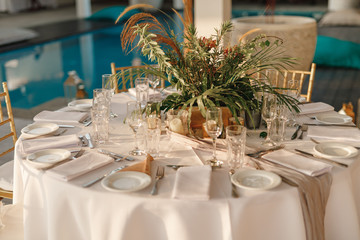 Romantic wedding table arrangement with beige tablecloth and napkins. Wedding. Banquet. The chairs and round table for guests, served with cutlery, flowers and crockery and covered with a tablecloth