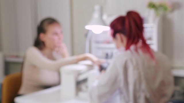 Woman manicurist with gloves in a beauty salon does a hardware manicure to a client before applying a gel coating. the image is out of focus