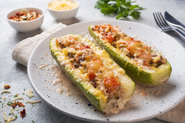 Baked stuffed zucchini boats with minced chicken mushrooms and vegetables with cheese on a plate.