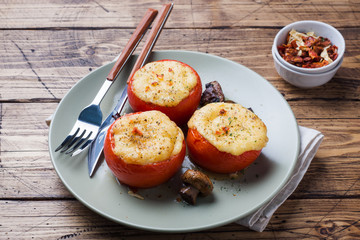 Baked whole tomatoes stuffed with mushrooms and cheese with seasonings on a wooden background.