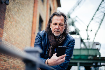 Older but cool man with beard and long grey hair uses a mobile phone in an urban environment