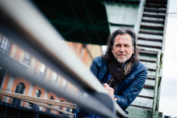 Older man in modern outfit leaning against a parapet in an urban environment