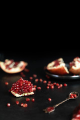 Some red juicy pomegranate, whole and broken, on a dark rustic wooden table.