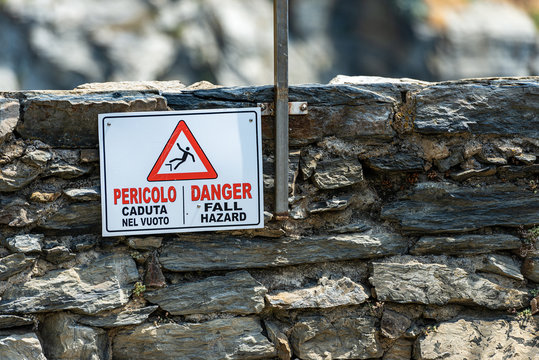 Warning sign whit the text, Danger Fall Hazard in English and Italian (Pericolo caduta nel vuoto) on a wall overlooking the sea cliff. Vernazza, Cinque Terre, Liguria, Italy