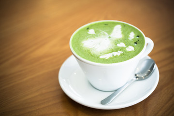cup of hot matcha latte with spoon on the wood table. Image has shallow depth of field.