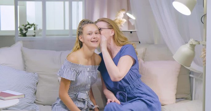 Adult happy daughter whispering a secret or positive news to mother's ear. Respectful relationships between different family generations