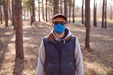 A lonely man in a tracksuit stands near the pines in a blue mask, cap and glasses