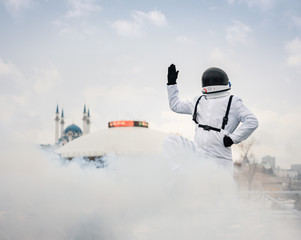 An astronaut in a spacesuit raised his hand up and greets earthlings against