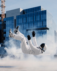 An astronaut in a spacesuit swims and flies against the backdrop of urban architecture buildings in a cloud of smoke.