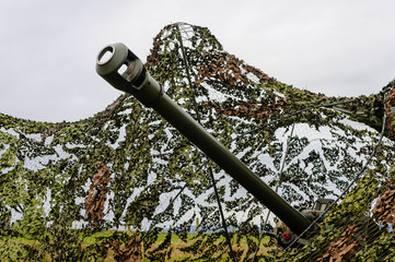 Muzzle of a 105mm Light Artillery Gun pokes through camouflage netting in a field