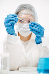 woman doctor in protective gloves dripping blue liquid onto glass slide with pipette making coronavirus test in lab