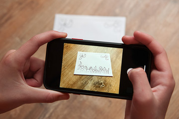 Child takes a photo easter card by mobilephone. Few painted rabbits are on a white card.