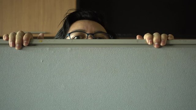 Asian man appeared suspiciously behind the partition as if he had done something wrong or stealing things in the office