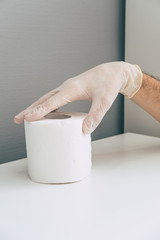 A medical worker in rubber latex glove on his hand holds toilet paper roll . Concept of coronavirus panic. Isometric and geometric style in the corner.