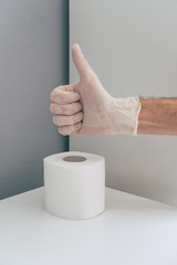 A medical worker in rubber latex glove on his hand near the toilet paper roll shows Okay or Like sign. Concept of coronavirus panic. Isometric and geometric style in the corner.