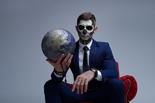 Satan holds the world in his hands. Planet earth in the hands of death. Man With Body Art Skeleton. Portrait of a skeleton in a suit looking at the camera.