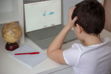 A preteen schoolboy in a white T-shirt, tired of sitting at the monitor with a laptop