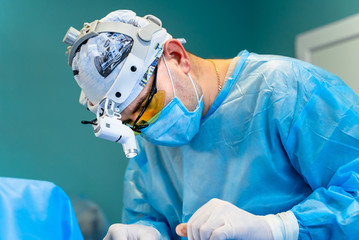 Surgeon performing cosmetic surgery in hospital operating room. Surgeon in mask wearing surgical...