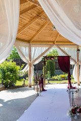 Decorative arch for the wedding ceremony of the newlyweds. Burgundy curtains and beautiful flowers.