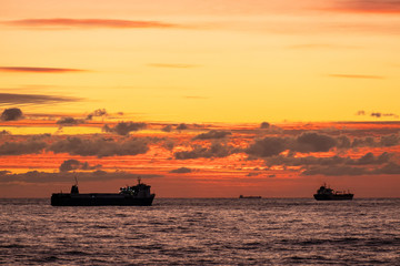 Sunset over the sea. A naval ship on the horizon. Oil tanker ship at sea on a background of sunset sky