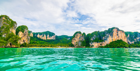 Fototapeta na wymiar View from boat going to famous Railay beach, Krabi Thailand. Coastline of Andaman sea, famous tourist and backpacker target. Tropical paradise, exotic vacation. Cloudy weather in summer day