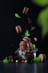 Macaroons with nuts and pieces of chocolate fall into a vintage vase.Photo on a black background....