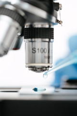 drop of light blue liquid on glass slide under modern microscope and pipette to make coronavirus test in lab closeup