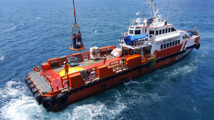 Songkhla, Thailand-February 27, 2020 : Red Supply boat transfer worker and cargo by personnel basket from platform to supply boat of oil and gas industry 
