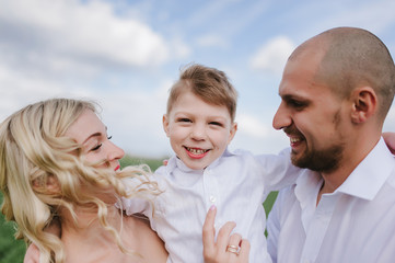 Fototapeta premium Family on a walk in a field with green grass and blue sky, early spring, good weather, happy family, white clothes