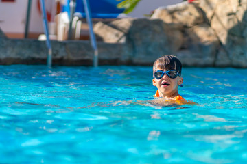 A happy boy in swimming goggles and arm ruffles in an outdoor pool. The child learns to swim. Family holidays at a tropical resort.