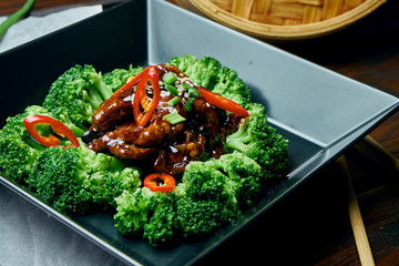 Serving of fresh boiled broccoli with chicken in teriyaki sauce and chili peppers in a black bowl...
