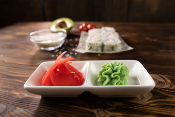 wasabi and ginger on a white plate with rolls on a blurry background