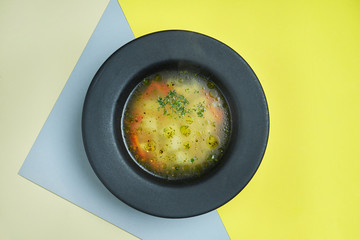 Dietary and healthy chicken stock with vegetables in a black bowl on a colored background. Close up view